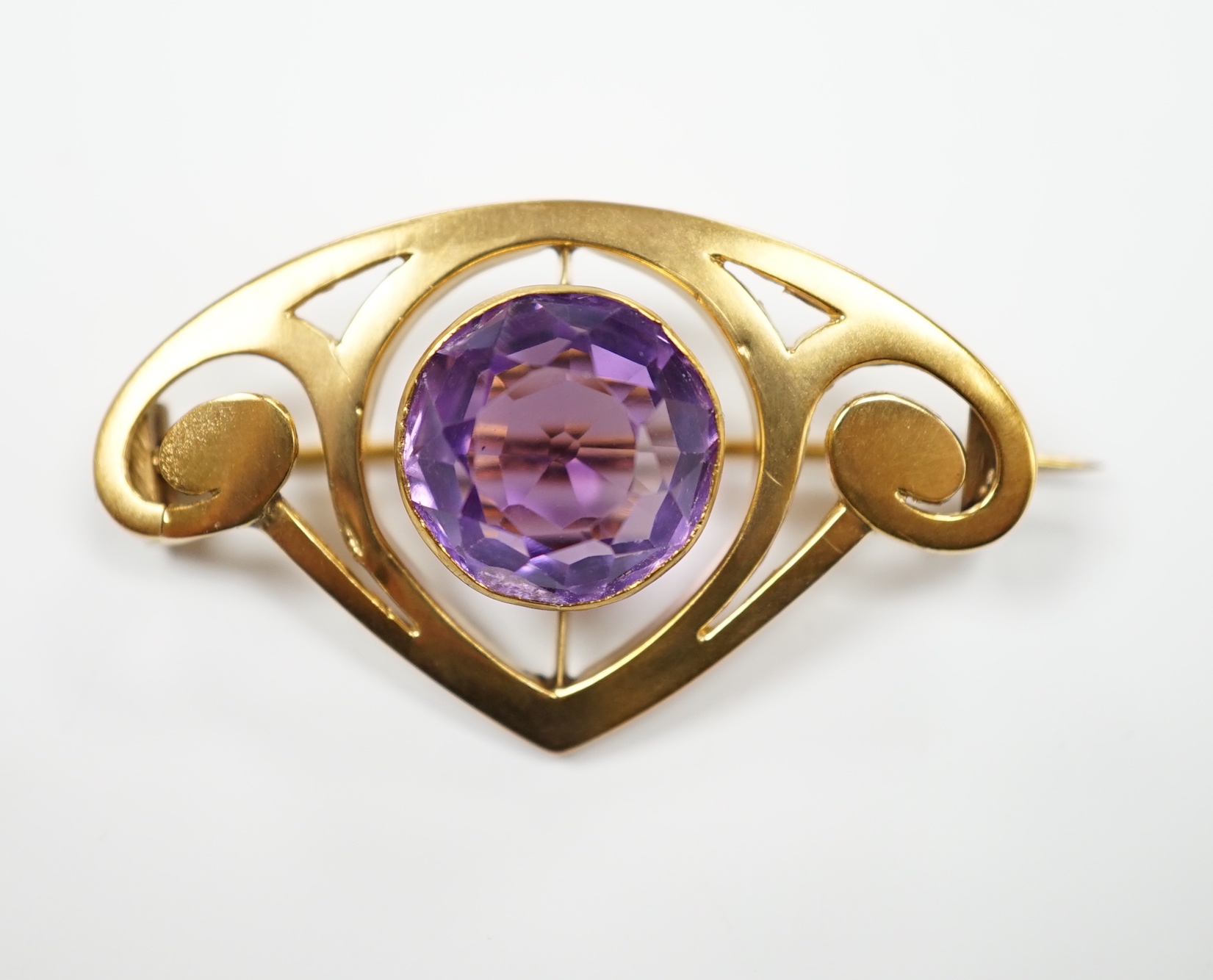 An Art Nouveau style yellow metal and single stone round cut amethyst set brooch, 35mm, gross weight 3.4 grams.